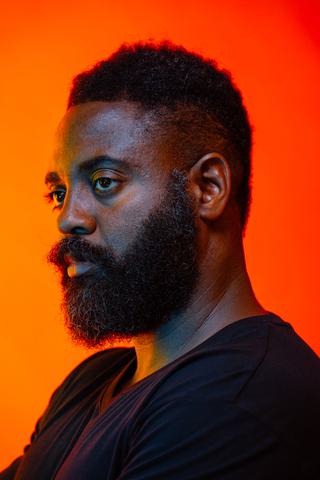 Portrait of Reginald Dwayne Betts on a warm red/orange background